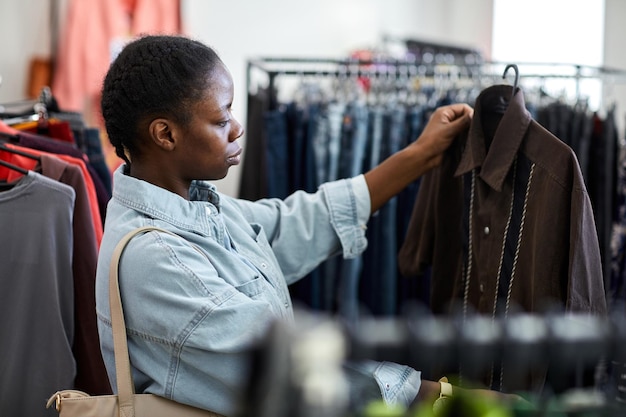 Retrato de vista lateral de una joven negra mirando ropa en una tienda de segunda mano
