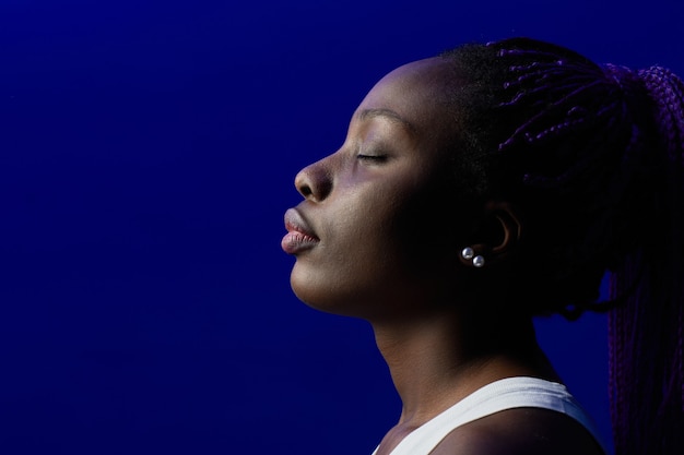 Retrato de vista lateral mínima de la joven mujer afroamericana con los ojos cerrados contra el fondo púrpura en el estudio, espacio de copia