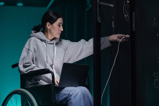 Retrato de vista lateral de una mujer discapacitada en silla de ruedas que trabaja con una red de supercomputadoras en la sala de servidores, concepto de trabajo accesible, espacio de copia