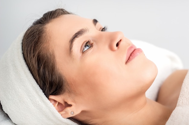 Retrato de vista lateral de una mujer joven pensativa acostado en la mesa de esteticista mientras espera el procedimiento cosmético en el salón de belleza