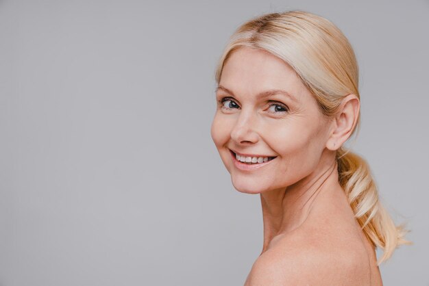 Foto retrato de vista lateral de una mujer rubia madura de buen aspecto con piel limpia sonriendo aislada sobre un fondo gris