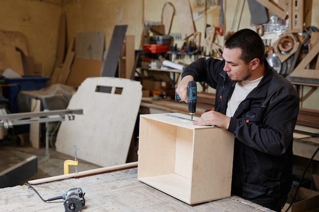 Retrato de vista lateral del trabajador masculino construyendo muebles de madera en el espacio de copia del taller de fábrica