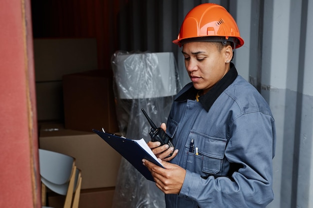 Retrato de vista lateral de una trabajadora multiétnica que usa casco mientras revisa los contenedores en el barco