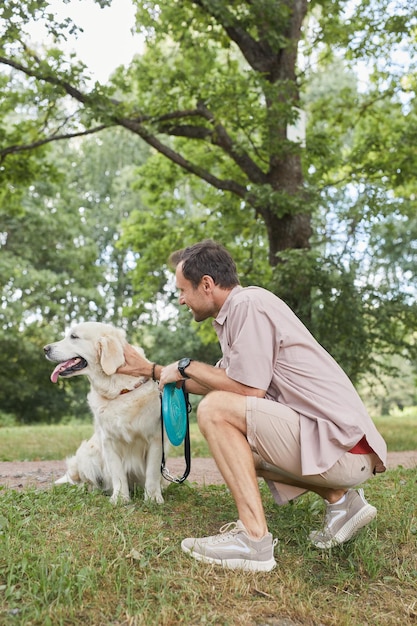 Retrato de vista lateral vertical de hombre feliz jugando con perro al aire libre en verano en el parque verde