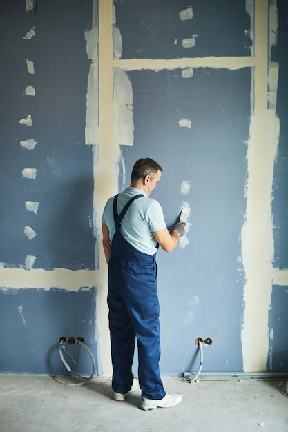 Retrato de vista posterior de cuerpo entero del hombre mayor que trabaja en la pared seca mientras se renueva la casa, espacio de copia