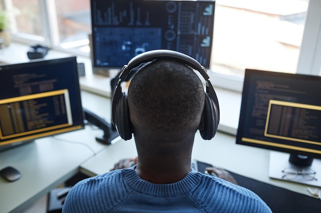 Retrato de vista posterior del desarrollador de software en la estación de trabajo con múltiples pantallas de computadora