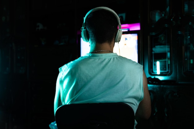 retrato de la vista posterior de un jugador con auriculares jugando juegos en línea en su habitación