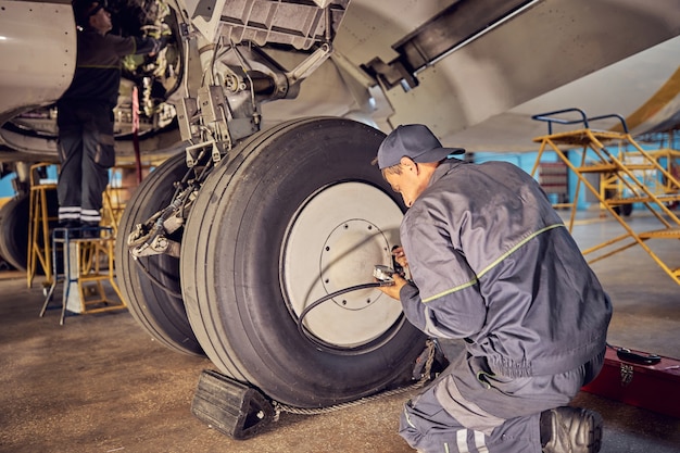 Retrato de vista posterior del técnico de tierra que trabaja en el aeropuerto arreglando aviones y comprobando el tren de aterrizaje