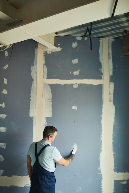 Foto retrato de vista posterior vertical del hombre mayor que trabaja en la pared seca mientras se renueva la casa, espacio de copia