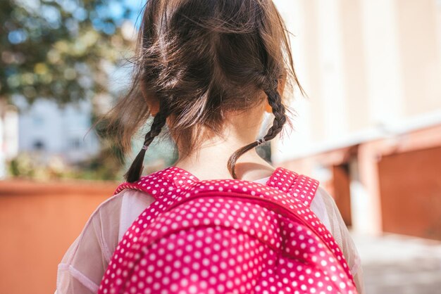 Retrato de vista trasera de primer plano de una linda niña en edad preescolar posando al aire libre con una mochila rosa contra un edificio borroso Niña feliz caminando después de aprender lecciones escolares Educación de personas
