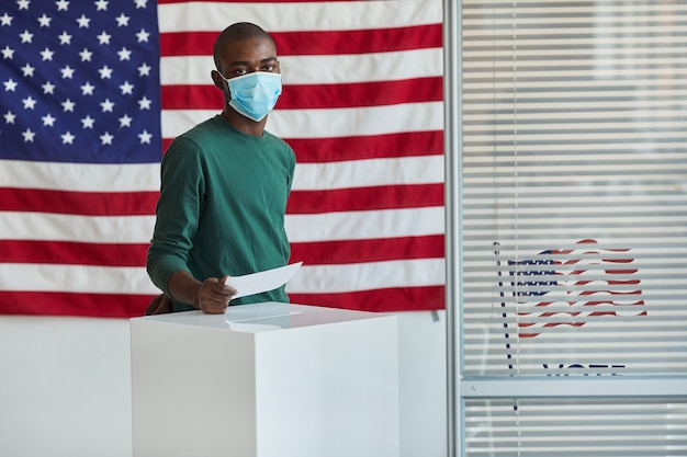 Retrato de votante africano con máscara protectora votando en el colegio electoral estadounidense durante la pandemia