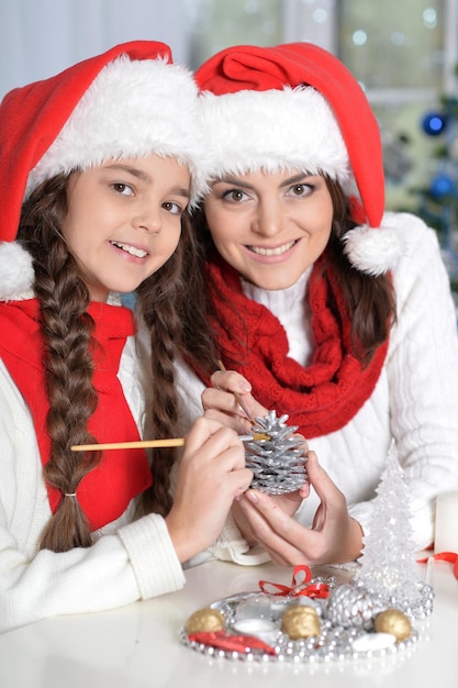 Retrato de ypung madre y su hija haciendo adornos navideños sentados a la mesa