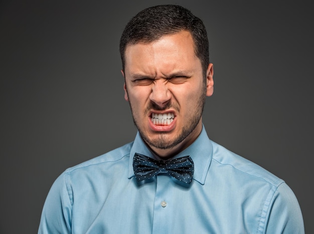 Retrato zangado chateado jovem de camisa azul, gravata borboleta