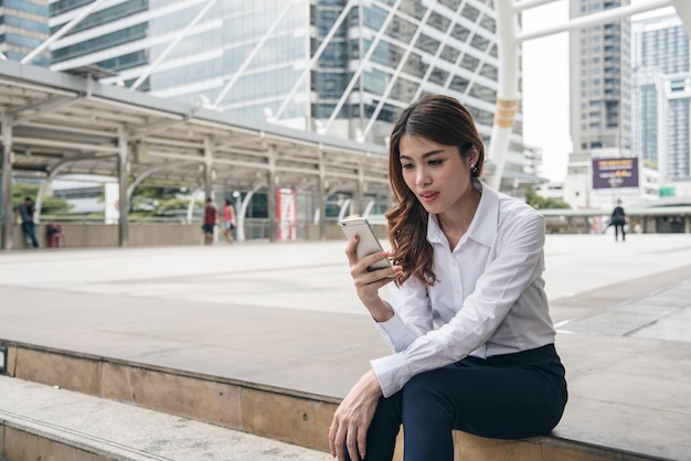 Los retratos de la confianza asiática hermosa de la mirada de la mujer están sosteniendo el teléfono móvil.