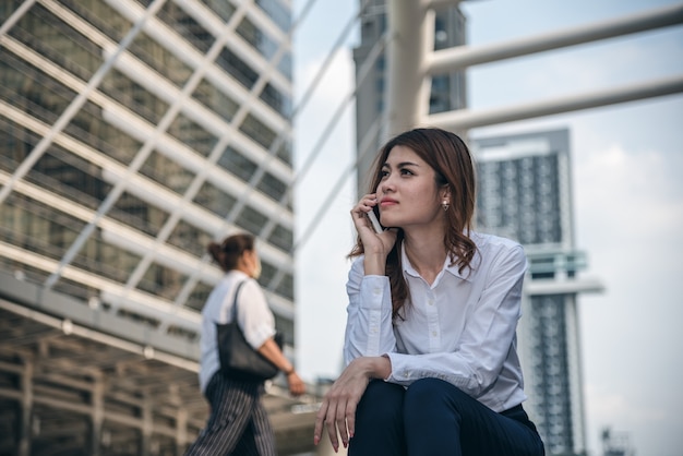 Los retratos de la confianza hermosa de la mirada de la mujer asiática están de pie y están sosteniendo el teléfono móvil