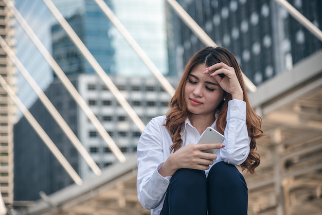 Retratos da bela mulher asiática estão segurando o sentimento de sensação de telefone inteligente pela depressão urbana.