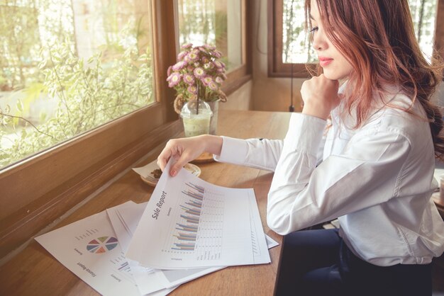 Retratos de mulher asiática bonita na expressão de pensamento trabalhando com documento de gráfico financeiro