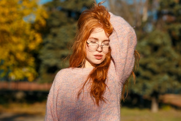 Retratos de uma encantadora garota ruiva com um rosto bonito. garota posando no parque outono em um suéter e uma saia de cor coral. a menina tem um humor maravilhoso