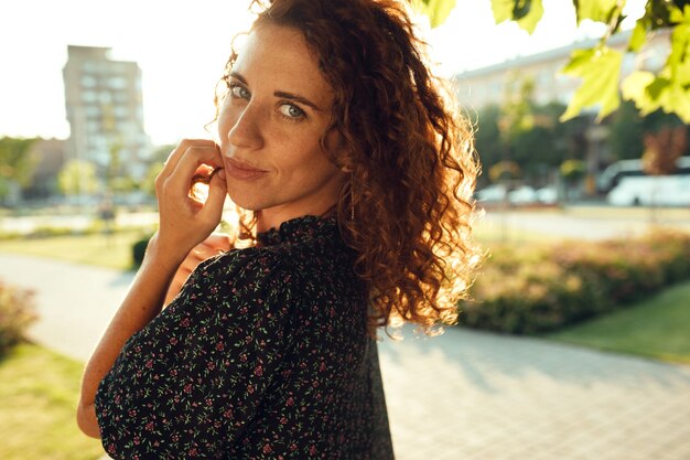 Retratos de una encantadora chica pelirroja con pecas y una cara bonita. La niña posa para la cámara en el centro de la ciudad. Ella tiene un gran humor y una dulce sonrisa.