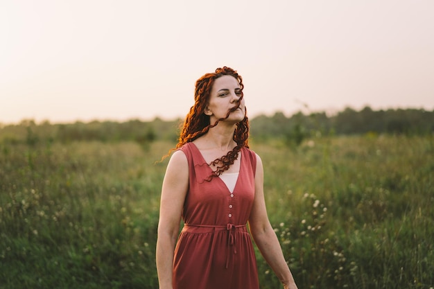 Retratos de una encantadora mujer pelirroja con una cara linda Chica posando para la cámara en el campo al atardecer