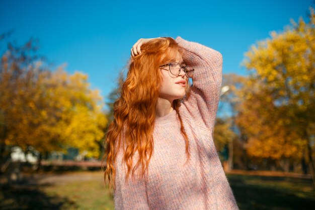 Retratos de una encantadora pelirroja con una linda cara. Chica posando en el parque otoño en un suéter y una falda de color coral. La chica tiene un humor maravilloso