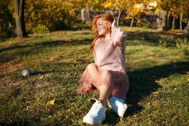 Retratos de una encantadora pelirroja con una linda cara. Chica posando en el parque otoño en un suéter y una falda de color coral. La chica tiene un humor maravilloso
