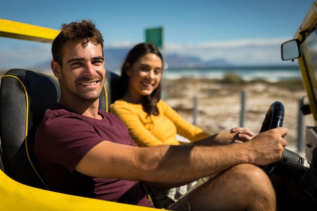 Retratos de una feliz pareja caucásica mirando a la cámara sentada en un buggy de playa junto al mar hablando. descanso en la playa en un viaje por carretera de vacaciones de verano.