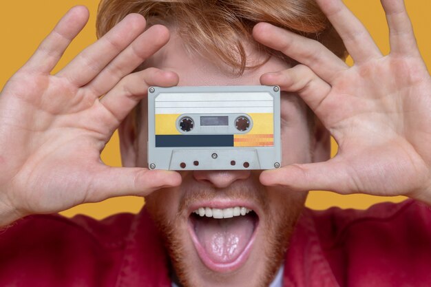 Foto retro. cerca del joven jengibre en chaqueta roja sosteniendo un cassette