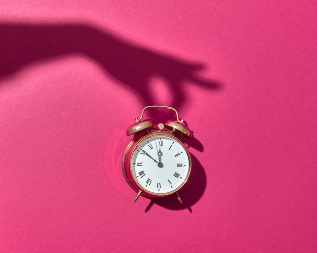 Retro Cooper Wecker mit harten Schatten von der Hand der Frau auf einem heißen rosa Hintergrund, Kopienraum.