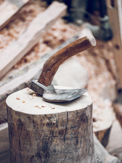 Retro-Dechselwerkzeug mit Schneide und Holzgriff zum Schnitzen von Holz, das auf einem Holzstumpf mit Rasur in der Landschaft platziert wird