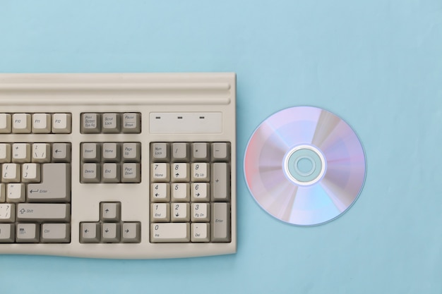 Retro-Elektronik, PC-Technologie der 90er Jahre. PC-Tastatur, CD auf blauem Hintergrund. Ansicht von oben