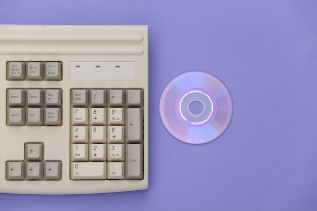 Retro-Elektronik, PC-Technologie der 90er Jahre. PC-Tastatur, CD auf lila Hintergrund. Ansicht von oben