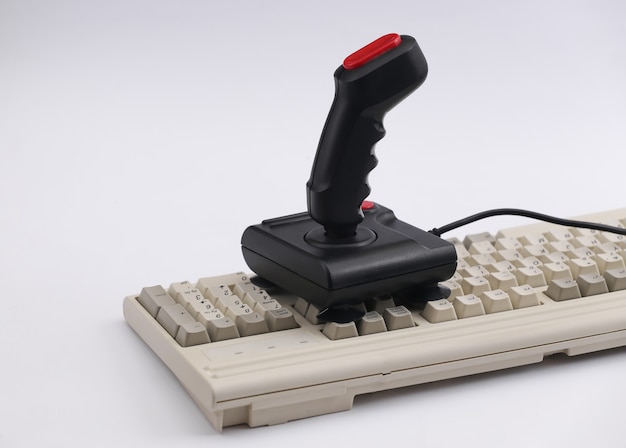 Retro-Joystick auf alter PC-Tastatur. Weißer Hintergrund. Attribute 80er, Gaming