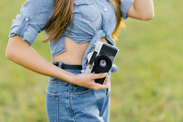 Retro- Kamera in den Händen eines Mädchens in der Denimkleidung. Der Reisende oder Reiseblogger mit einer Kamera