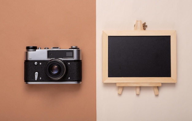 Retro-Kamera und leere Mini-Kreidetafel mit Kopierraum auf braun-beigem Hintergrund