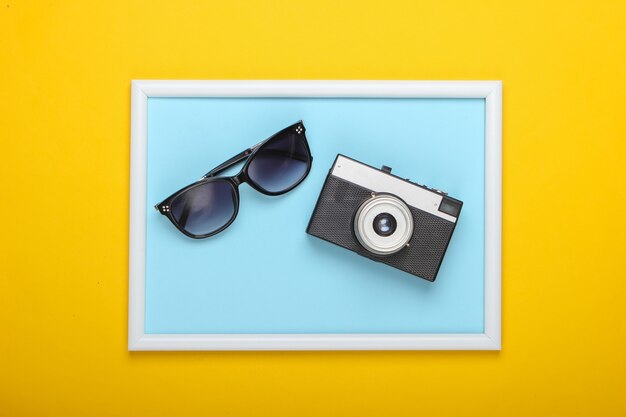 Retro-Kamera und Sonnenbrille auf gelber Oberfläche mit Fotorahmen