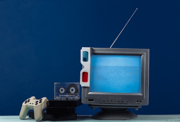 Retro-Medien, Unterhaltung 80er Jahre. Antenne altmodischer Retro-TV-Empfänger, Anaglyphen-Stereobrille, Audio- und Videokassette, Gamepad auf klassischem Blau.