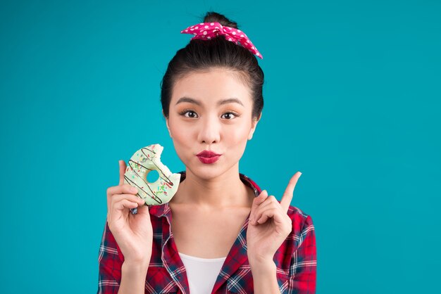 Retro mujer alegre disfrutar de dulces, postres de pie sobre fondo azul.