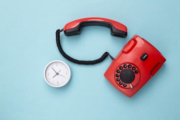 Retro rotes altmodisches Telefon mit Wählscheibe und Uhr auf Draufsicht des blauen Hintergrundes