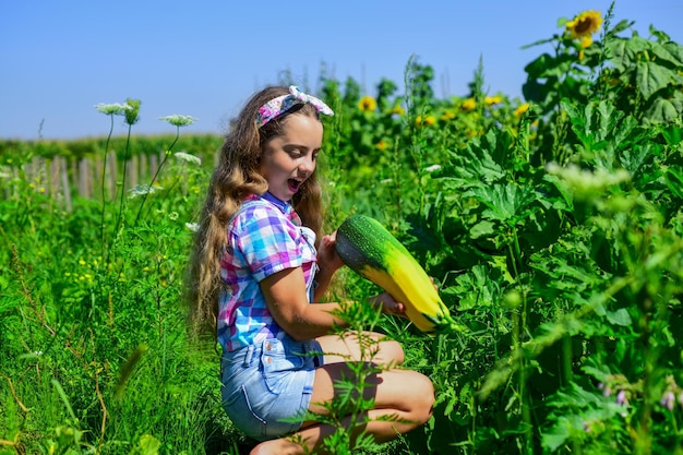 Retro schönes Mädchen zeigt Zucchini hübsches Kind auf dem Bauernhof Schönheit der Sommernatur kleines Mädchen auf dem landwirtschaftlichen Garten mit Squash wachsendem Gemüsemark glückliche Kindheit Umpflanzen von Pflanzen