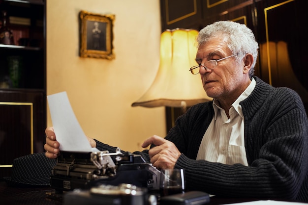 Retro-Senior-Mann-Autor mit Brille, der auf veralteter Schreibmaschine schreibt.