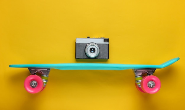 Retro-Stil. Kunststoff-Mini-Kreuzer-Brett und Retro-Kamera auf gelbem Hintergrund. Pastellfarbentrend. Sommerspaß. Jugend minimalistisches Konzept.