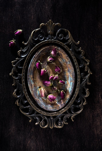 Retro-Stillleben mit getrockneten Rosenblüten auf einem metallischen antiken Tablett und Draufsicht auf einen Bronzerahmen