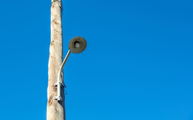 Retro-Straßenlampe, die an einem elektrischen Holzpfahl hängt Vintage-Säulenlampe mit blauem Himmel im Hintergrund