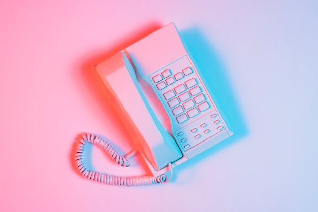 Retro telefono rosa con luz azul sobre superficie rosa