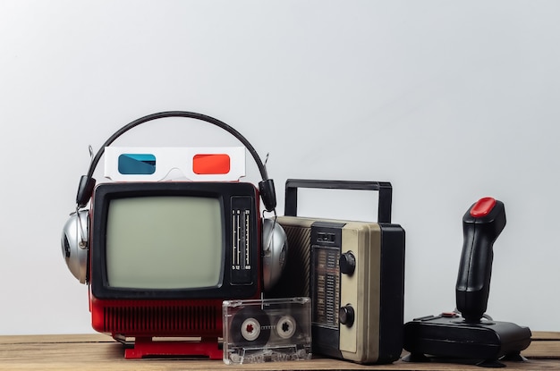 Retro tragbarer Mini-Fernseher mit Kopfhörern, 3D-Brille, Funkempfänger, Joystick, Audiokassette auf weißem Hintergrund. Attribute 80er, Retro-Stil