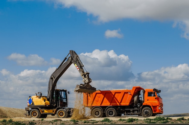 Una retroexcavadora amarilla carga la tierra en un camión durante la construcción de una carretera contra el cielo