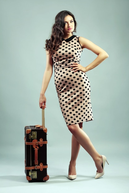 Retrostilfoto der jungen Frau mit Koffer auf grauem Hintergrund