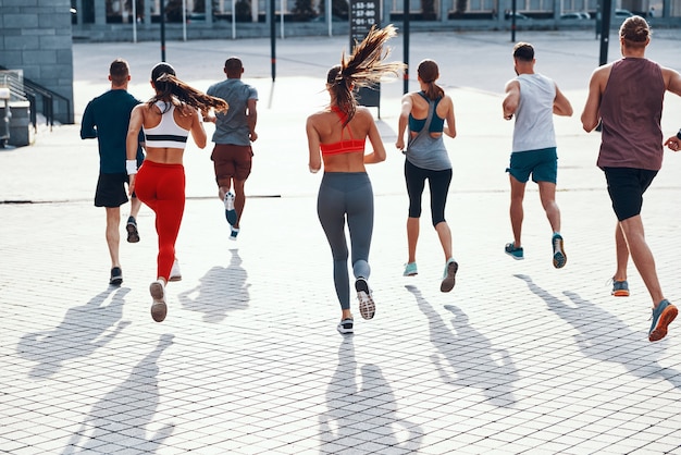 Foto retrovisor de corpo inteiro de pessoas em roupas esportivas correndo enquanto se exercitam na calçada ao ar livre