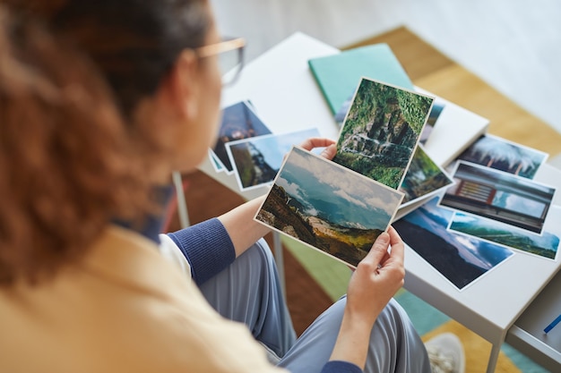 Retrovisor de mulher escolhendo as fotos para colagem ou fazendo um mapa dos desejos à mesa